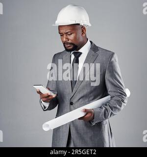The boss is always on call. a well-dressed civil engineer using his cellphone while standing in the studio. Stock Photo