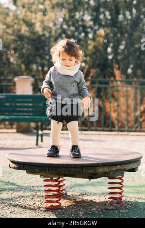 Outdoor portrait of adorable toddler girl having fun on playground, 1 - 2 year old kid playing in park Stock Photo