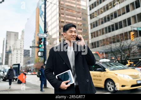 Young busy happy Asian business man walking on city street making phone call. Stock Photo