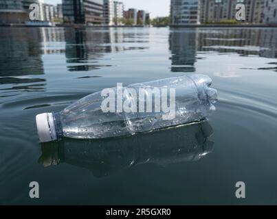 Environmental pollution - plastic bottle floating in sea water in urban city. Modern residential buildings in the background. Close up image with copy Stock Photo