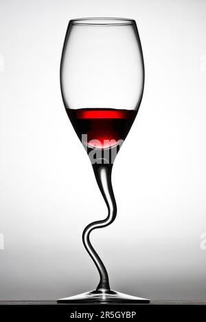 Curved wine glass filled with red wine against a white background Stock Photo