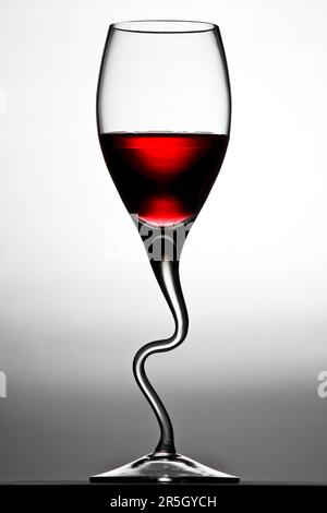 Curved wine glass filled with red wine against a white background Stock Photo