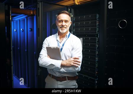 Performing regular maintenance on all machinery. Portrait of a mature man holding a digital tablet while working in a server room. Stock Photo