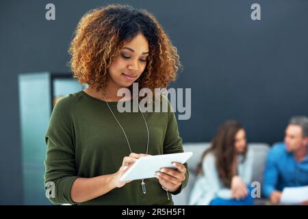 Staying current on industry related developments. a young businesswoman using a digital tablet with her team in the background. Stock Photo