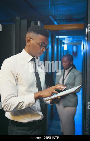 We make sure to have each others back. two young IT specialists standing together in the server room and using technology. Stock Photo