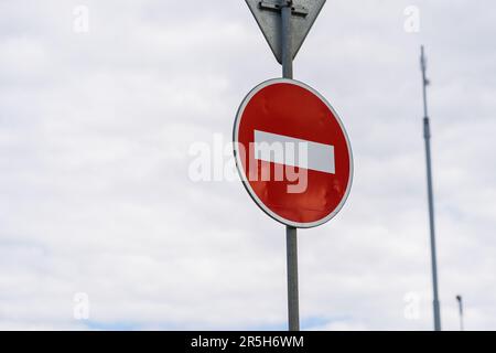 A photo of a 'No entry' road sign against the backdrop of the sky. The sign consists of a red circle with a white horizontal rectangle in the center. Stock Photo