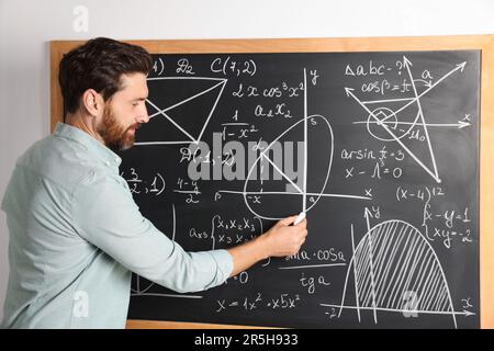 Mature teacher explaining mathematics at chalkboard in classroom Stock Photo