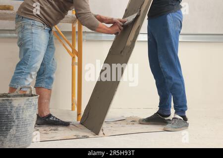 Worker spreading adhesive mix over tile with spatula, closeup Stock Photo