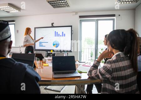 A businesswoman explains graphs to her colleagues in an international meeting Stock Photo