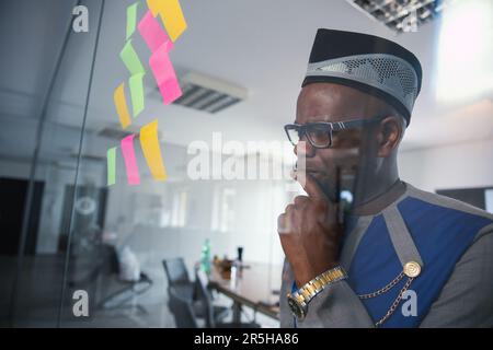 An African businessman looks thoughtfully at the sticky notes hanging on the wall Stock Photo