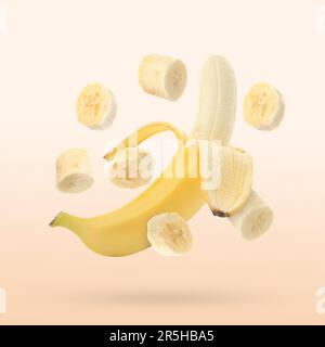 Delicious whole and cut banana fruits falling on light beige background Stock Photo