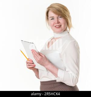 Portrait of sincere smiling and happy 49-year-old blonde businesswoman holding clipboard and pencil in hands, wearing in white blouse Stock Photo