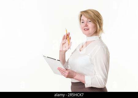 Blonde woman wearing in white blouse holding clipboard and pencil in hands, looking away and smiling. Waist up, studio shot against white background Stock Photo