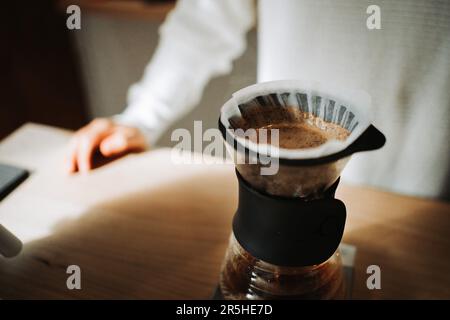 Unrecognizable young man preparing coffee using chemex pour over coffee maker and drip kettle, in a coffee shop Stock Photo