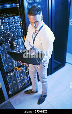 Boosting the capacity of high performance systems. High angle shot of a mature man using a laptop while working in a server room. Stock Photo