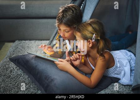 What are weekends without wifi. an adorable little boy and girl using a tablet together while chilling in a homemade tent in the living room at home. Stock Photo