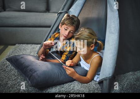 Learning new apps together. an adorable little boy and girl using a tablet together while chilling in a homemade tent in the living room at home. Stock Photo