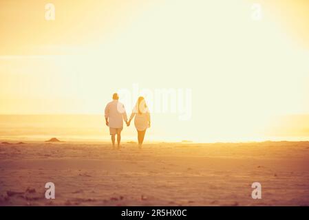 Letting the sun shine on their love. Rearview shot of an affectionate mature couple walking hand in hand on the beach. Stock Photo