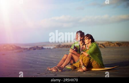 His music is so soothing. a young man playing the guitar while sitting on the beach with his girlfriend. Stock Photo