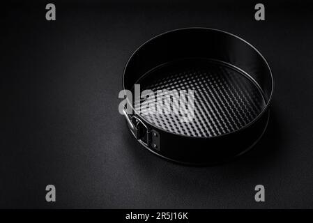 Round metal black detachable baking dish for baking on a dark concrete background Stock Photo