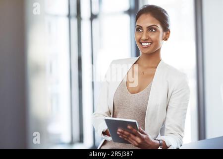 Technology that supports her business vision. a thoughtful young businesswoman using a digital tablet at work. Stock Photo