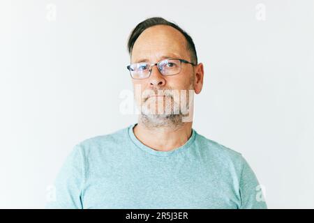 Close up portrait of middle age man wearing glasses and turquoise t-shirt, white background Stock Photo