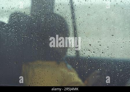 Sad young woman sitting lonely and depressed inside a car through raindrops on window Stock Photo
