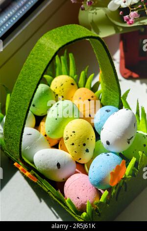 Easter green basket with plastic colored eggs on the windowsill Stock Photo