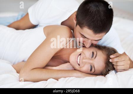Good morning. Attractive young woman smiling as her partner leans in to kiss her. Stock Photo