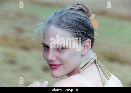 young slim pretty blonde haired woman in her early 20s posing for portrait in field 1990s Stock Photo
