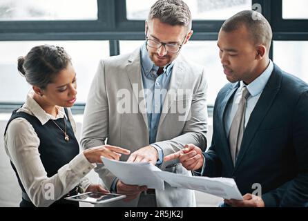 I need you to make some adjustments here...and here. three businesspeople looking over some paperwork in the office. Stock Photo