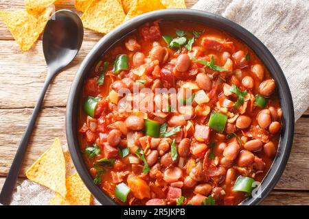 Mexican pinto bean stew with tomatoes, sausages, bacon and onions close-up on a bowl on the table. horizontal top view from above Stock Photo