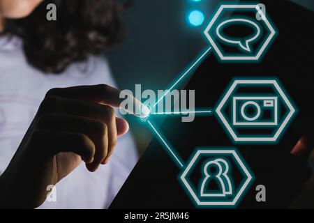 An unrecognizable girl going to touch digital tablet screen in a dark room with blue led lights. Some icons are floating. Stock Photo