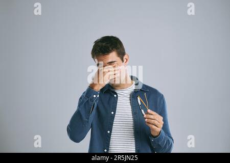 Maybe these glasses are whats hurting my eyes. a man suffering from a headache against while posing against a grey background. Stock Photo