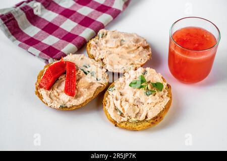 Salmon spread with fresh cheese on three sliced bread, glass of fresh juice, checkered cloth on white background. Stock Photo