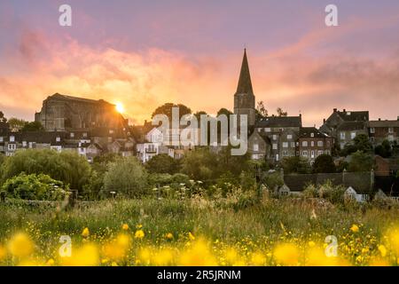 Sunday 4th June 2023. Malmesbury, Wiltshire, England - The clouds melt away as the sun rises behind the historic abbey and a meadow of buttercups over Stock Photo