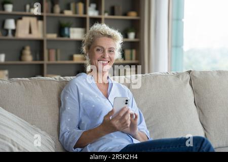 Positive beautiful blonde mature woman using mobile phone Stock Photo