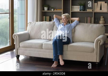 Dreamy positive mature woman relaxing on home sofa Stock Photo