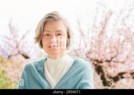 Spring portrait of beautiful and elegant middle age woman posing against pink blooming tree Stock Photo