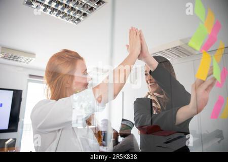 Two coworkers high-five each other during a meeting while writing on stick notes Stock Photo