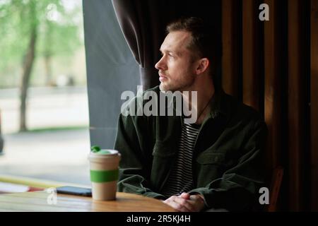 Young man sitting in a cafe on a coffee break. Looking at the window having good time in a small cafe High quality photo Stock Photo