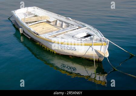Sibenik, Croatia - May 31, 2023: One old white weathered rowing boat tied up in calm sea water and its reflection Stock Photo