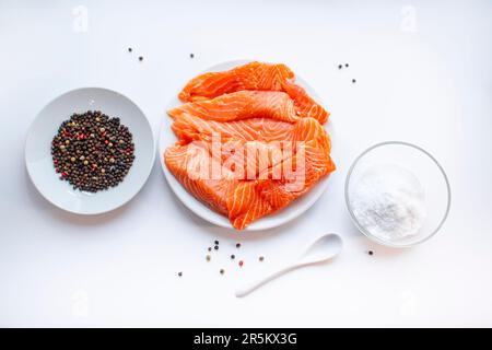 Fresh raw salmon fish fillet on a white plate, a small bowl of salt and black peppercorns on white background. Healthy food. Stock Photo