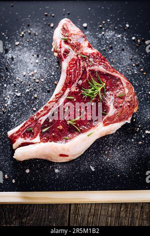 Raw cut of premium steak with bone. Rump steak with marble, dry aged, on a black background. Fresh Ribeye Steak. Stock Photo