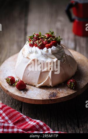 Pavlova cake decorated with strawberries on rustic wooden table surface. Cake is made from meringue and whipped cream Stock Photo