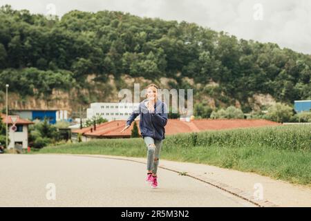 Kid girl running up the road, sporty child hurrying up fast Stock Photo