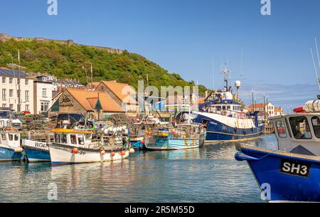 The harbour and town at Scarborough.  Boats are moored in the harbour with the waterfront behind. Castle ruins are on the hill above and the bow of a Stock Photo