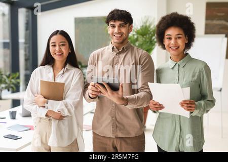 Successful Young Coworkers Holding Digital Tablet And Papers In Office Stock Photo