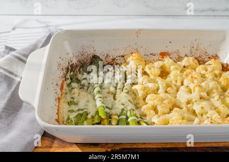 White ceramic baking dish with fresh baked asparagus and cauliflower. Delicious vegetables topped with garlic powder, and mozzarella cheese, close-up Stock Photo