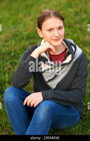 Outdoor portrait of cute young teen girl sitting on green fresh lawn Stock Photo
